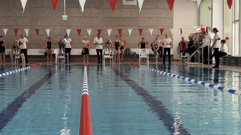 Innenaufnahme eines großen Schwimmbeckens mit mehreren Personen im und am Rand des Beckens.