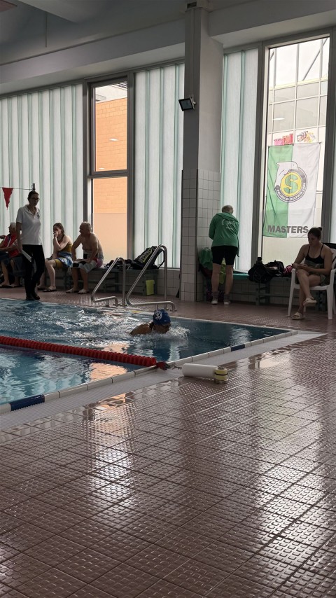 Innenansicht eines Schwimmbeckens mit mehreren Personen, die dort baden oder trainieren.