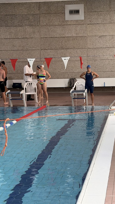 Innenaufnahme eines großen Schwimmbeckens mit mehreren Menschen im Becken und am Rand.