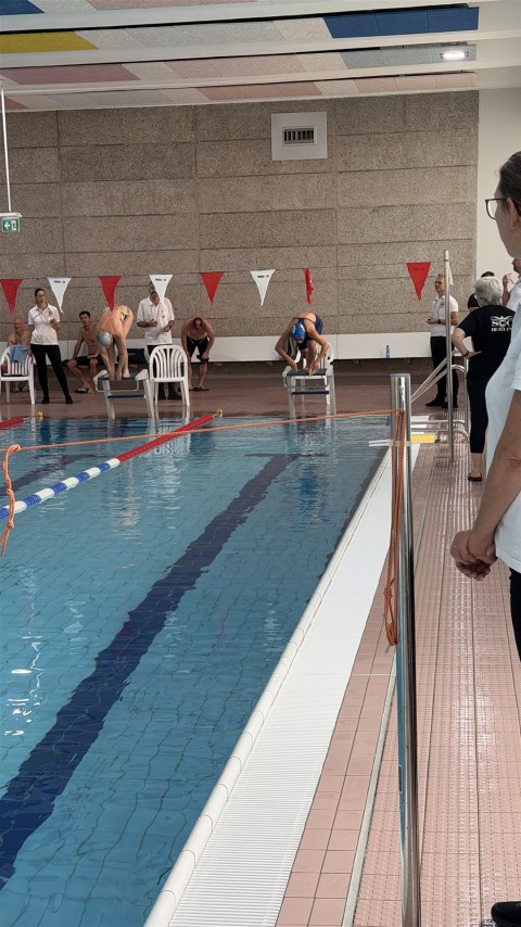 Innenansicht eines großen Schwimmbeckens mit mehreren Bahnen, auf dem mehrere Personen trainieren oder schwimmen.